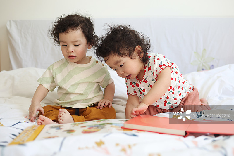 两个18个月大的中国双胞胎宝宝在父母的床上一起看书。图片素材
