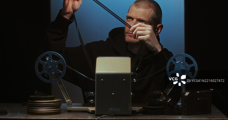 一位导演在电影的后台场景中将16毫米胶卷装载到模拟剪辑台上。图片素材
