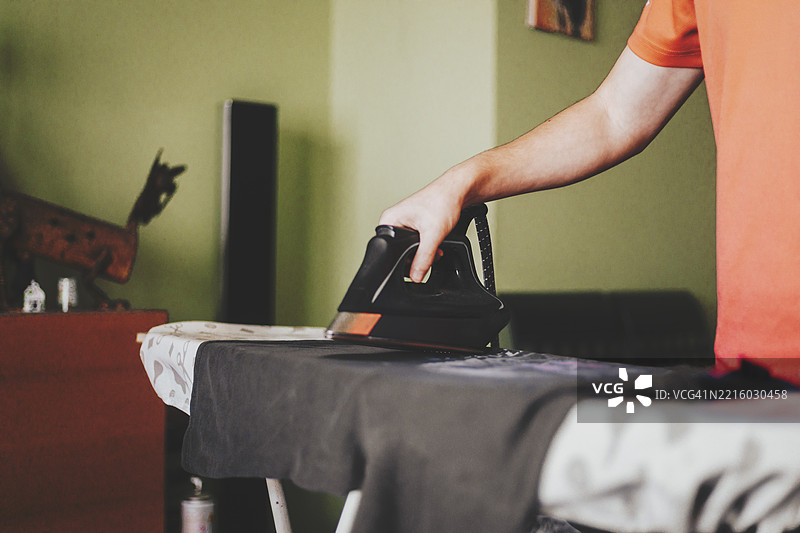 一个无法辨认的男人在家里熨烫一件灰色T恤。图片素材