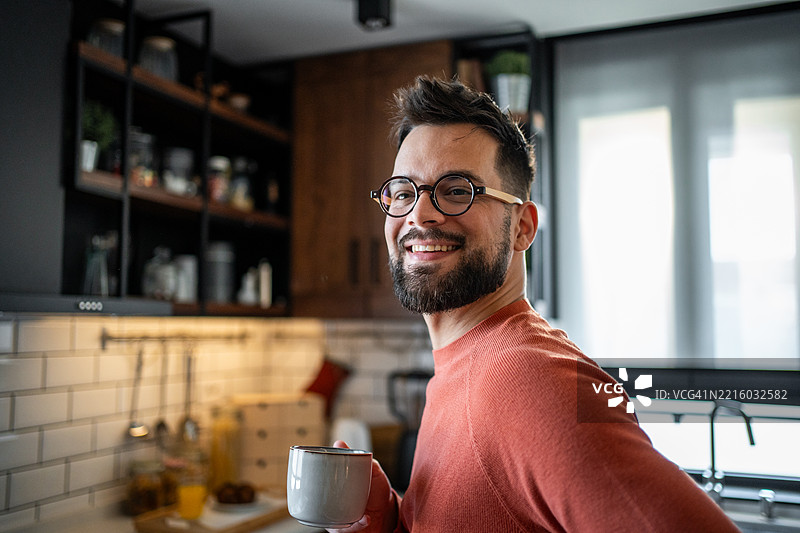 年轻男子在现代厨房里微笑着喝咖啡图片素材