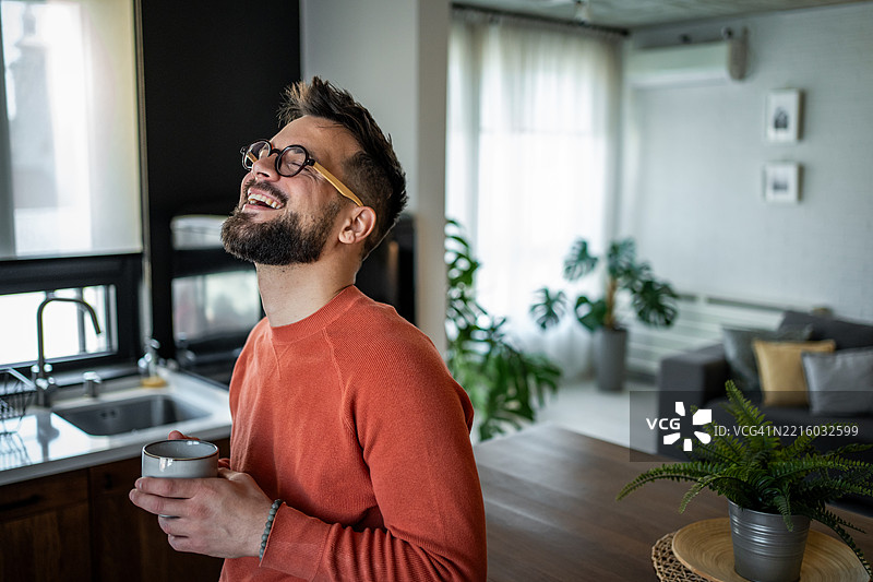 快乐的男人在家中拿着咖啡杯大笑图片素材