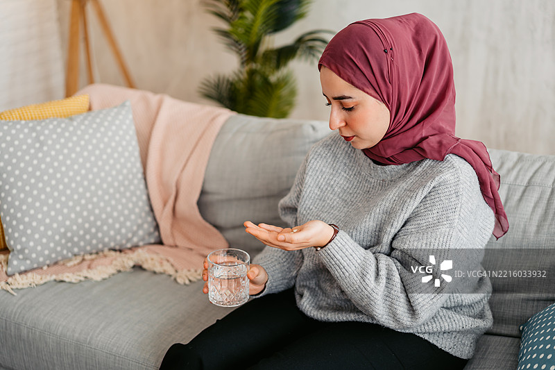年轻穆斯林女性在家中喝水服药图片素材