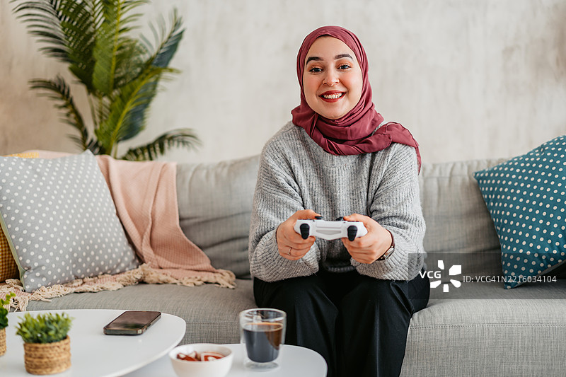 年轻穆斯林女性在家中用摇杆玩视频游戏图片素材