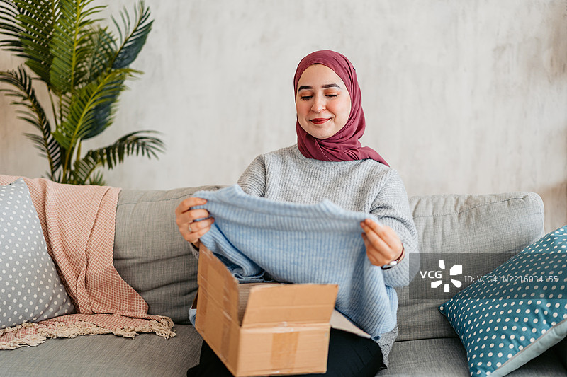 年轻穆斯林女性正在拆包裹，里面是她在线订购的新毛衣图片素材