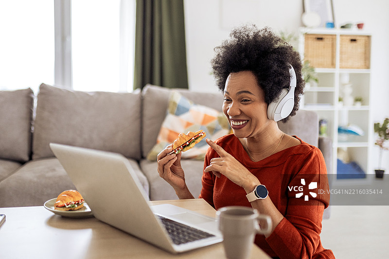 在视频通话中戴着耳机的女性一边吃新鲜的可颂面包一边工作图片素材