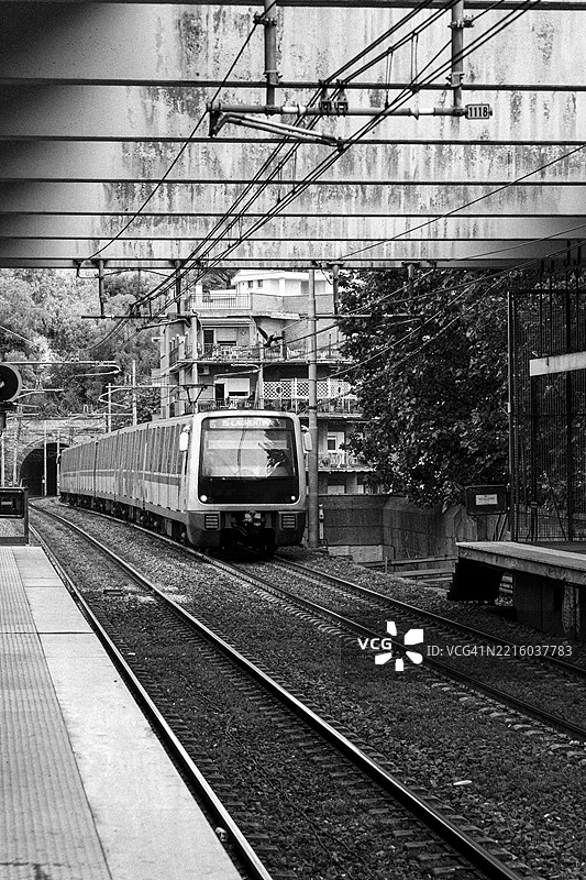 一列驶向圣劳伦蒂娜的列车在桥下经过，周围被住宅建筑和树木环绕，展示了城市铁路环境中结构化而又动态的运动。图片素材