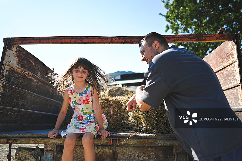 农民父亲和女儿在农场的拖车上玩 hay bale。图片素材