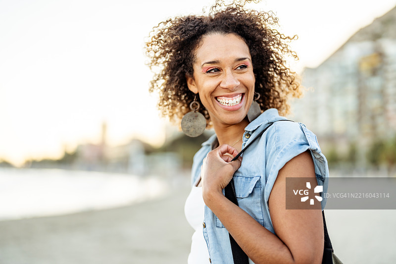 微笑的女性在日落时分享受沿着风景如画的海滩悠闲散步图片素材