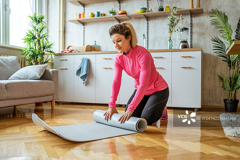 女性在家锻炼后卷起瑜伽垫图片素材