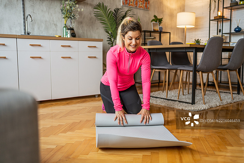 年轻女性在家锻炼后卷起瑜伽垫图片素材