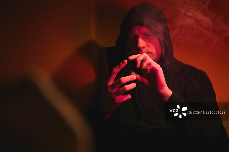 年轻男子在充满烟雾的红色灯光房间里浏览智能手机图片素材