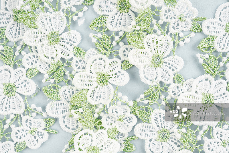 蓝色背景上的白色花朵和绿色叶子蕾丝织物。图片素材