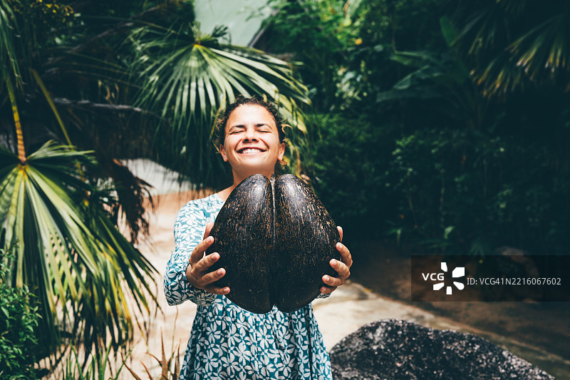 年轻女性手持巨型椰子海枣。图片素材