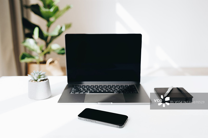 简约现代的工作空间，白色桌子上有笔记本电脑、智能手机、笔记本和植物。图片素材