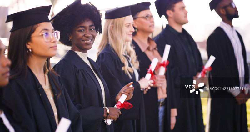 一群混合性别的学生穿着学位服，手持毕业证书。图片素材