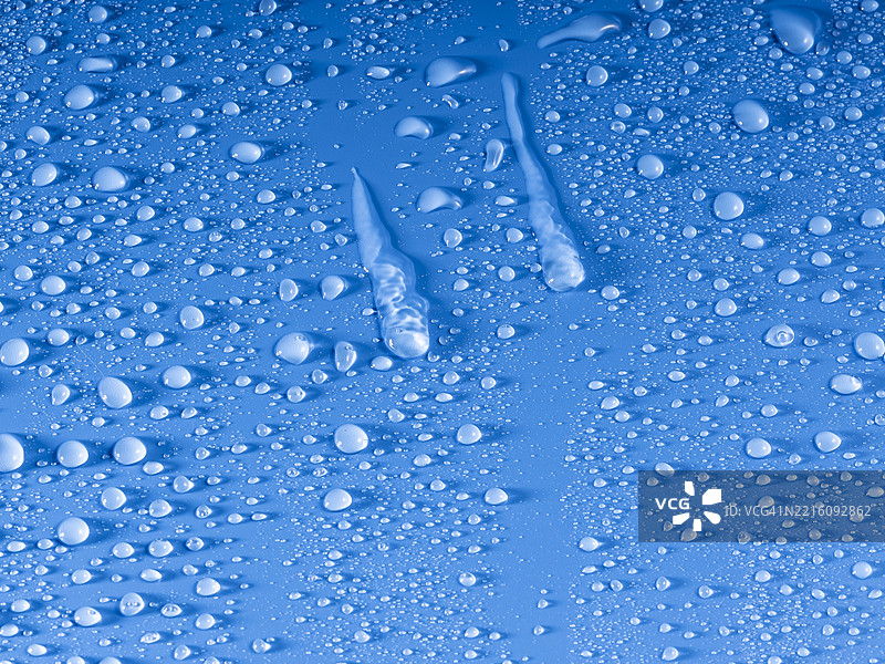湿润的表面上有透明的水滴在蓝色背景上滑动。图片素材