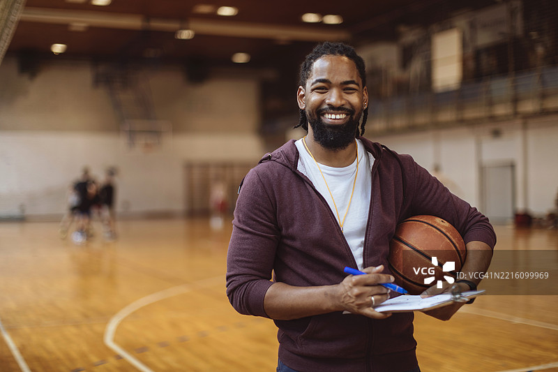 微笑的教练在室内篮球场上拿着篮球图片素材