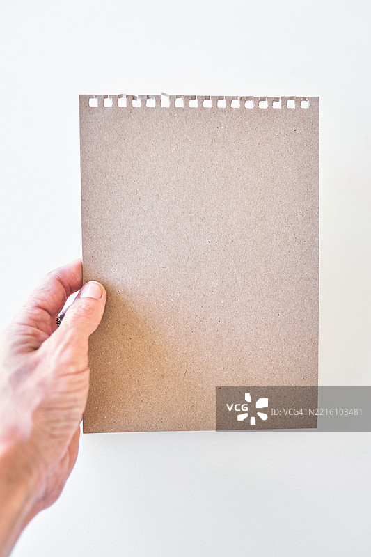 手握撕裂螺旋 perforation 的棕色牛皮纸，背景为白色图片素材