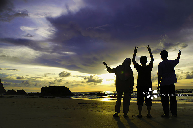 日落时分，朋友们在海滩上逆光而立，背景是天空的剪影。图片素材