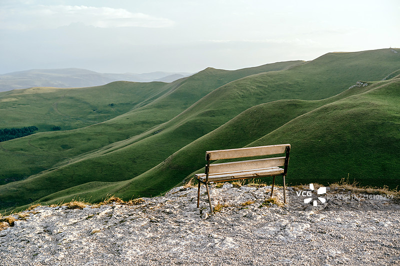 宁静的木长椅俯瞰着日落时分起伏的绿丘图片素材