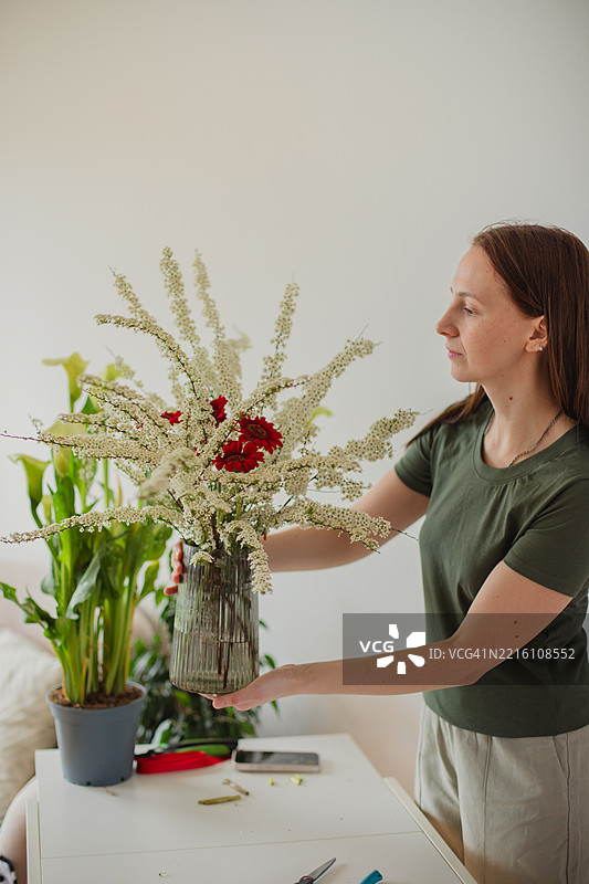 女人在家中桌子上整理花瓶里的花图片素材