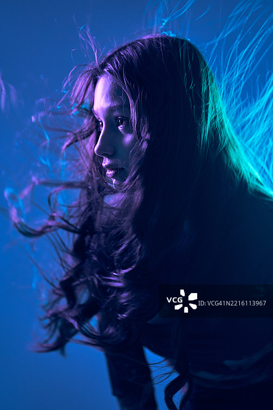 一个留着长发的少女在蓝紫色灯光下迎风回眸。图片素材
