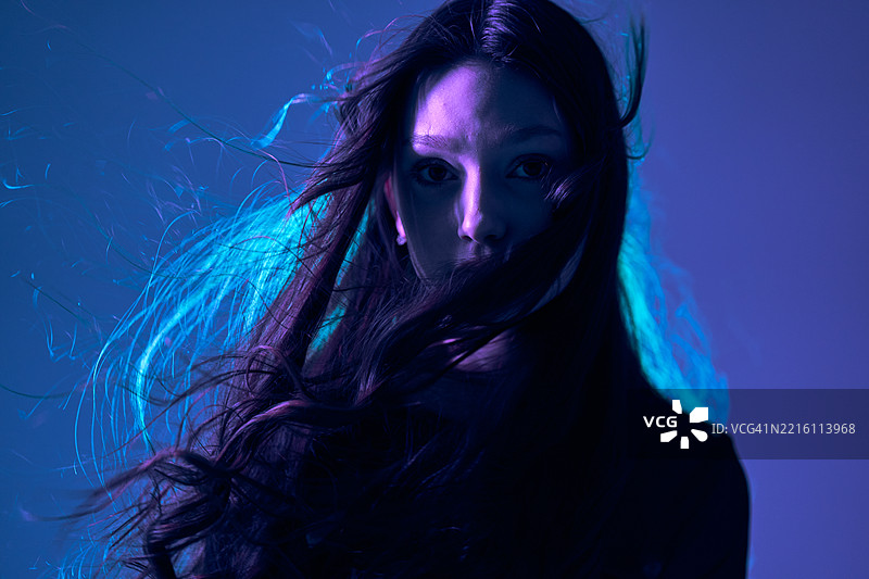 一位长发飘扬的少女在蓝紫色的光线下注视着镜头。图片素材