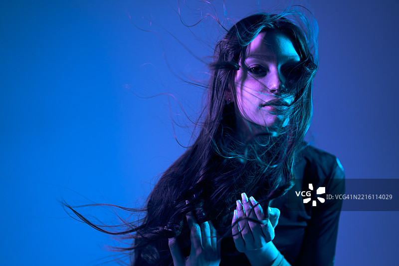 一位长发飘扬的少女在蓝紫色的光线下注视着镜头。图片素材