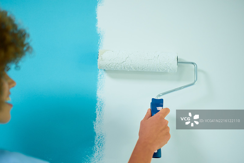 画家在浅蓝色墙壁上涂抹白色油漆图片素材