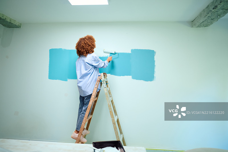 女人站在梯子上用滚筒给墙壁上漆图片素材