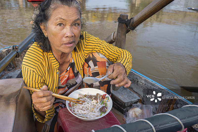 越南女性在湄公河三角洲的水上市场享用著名的米粉汤图片素材