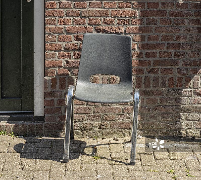 灰色塑料椅子配有金属框架，放置在石墙前的户外。图片素材