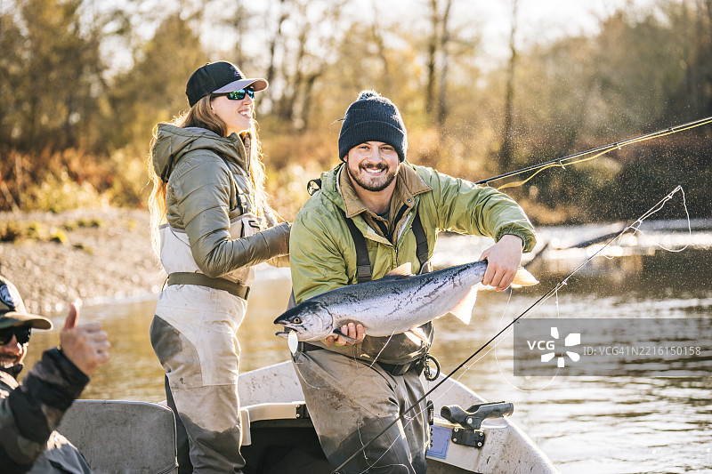 年轻男子在河上的小船上手持鲑鱼的肖像图片素材
