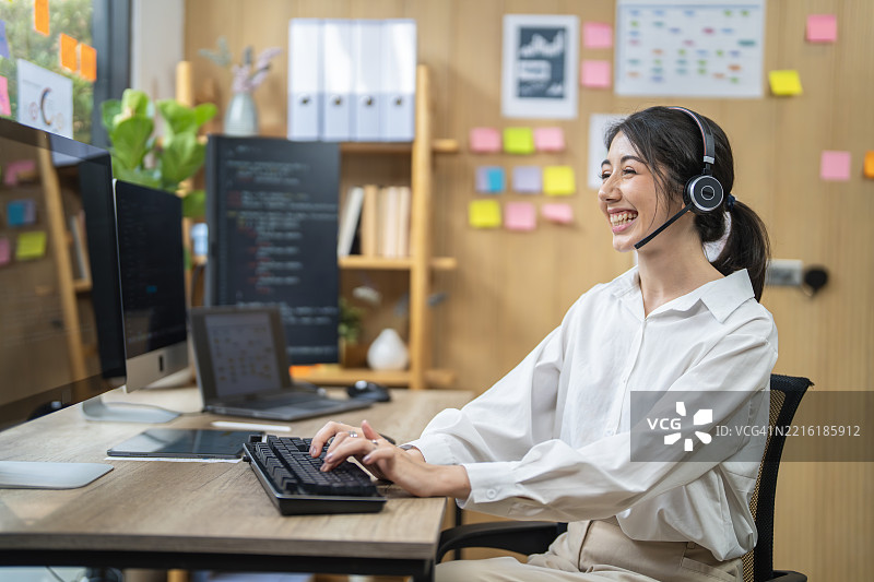 亚洲女商人在现代办公室佩戴耳机使用电脑工作图片素材