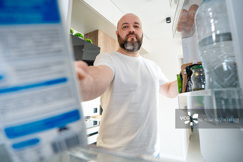 从冰箱视角查看的男人检查食品过期日期图片素材