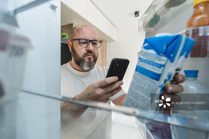 男子打开冰箱，用智能手机查看牛奶的保质期图片素材