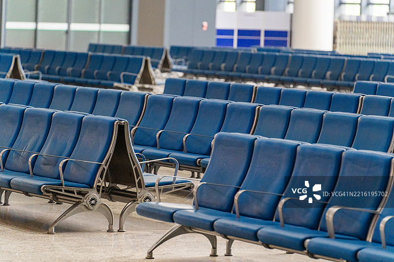 干净现代的机场候机区内，整齐排列的空蓝色椅子，营造出宁静有序的旅行环境。图片素材