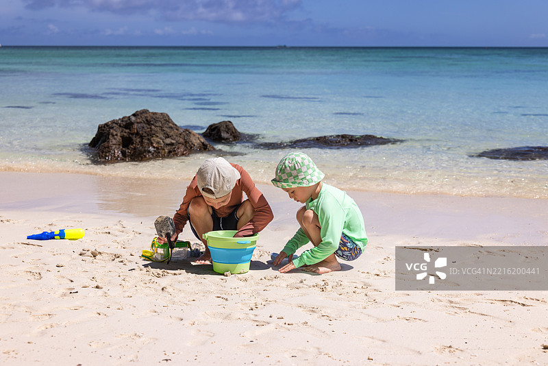 孩子们在热带海滩上用桶和沙滩玩具探索海洋生物图片素材