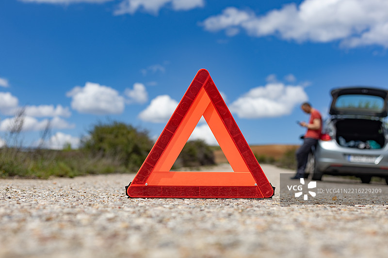 乡村道路上的警告三角架，旁边有一辆故障的汽车和司机图片素材