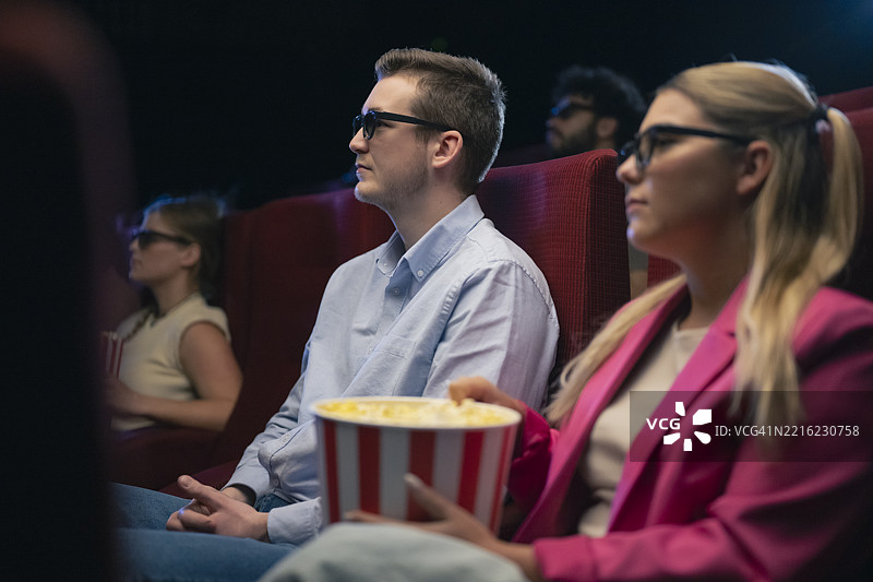 年轻的白人情侣在电影院享受3D电影，手里拿着爆米花图片素材
