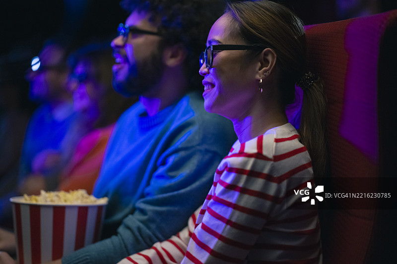 年轻的多种族情侣在昏暗的电影院里享受3D电影和爆米花图片素材