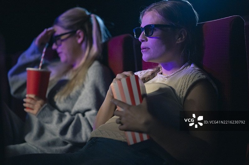 年轻的白人女性朋友们在舒适的电影院享受3D电影体验图片素材