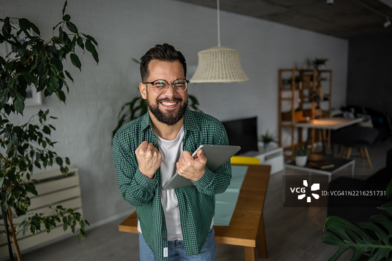 兴奋的年轻人在家中用平板电脑庆祝成功图片素材