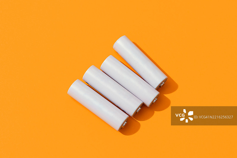 四个白色AA电池躺在橙色背景上图片素材