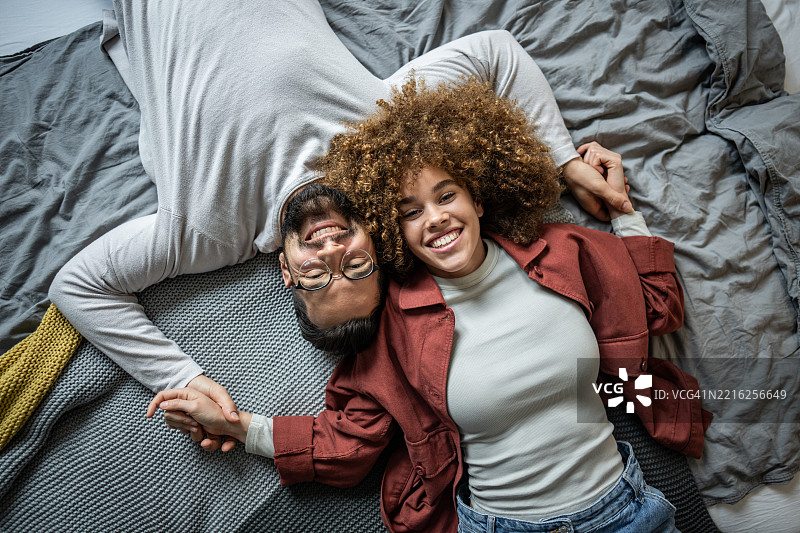 幸福的情侣躺在床上，手牵着手，微笑着看向镜头图片素材