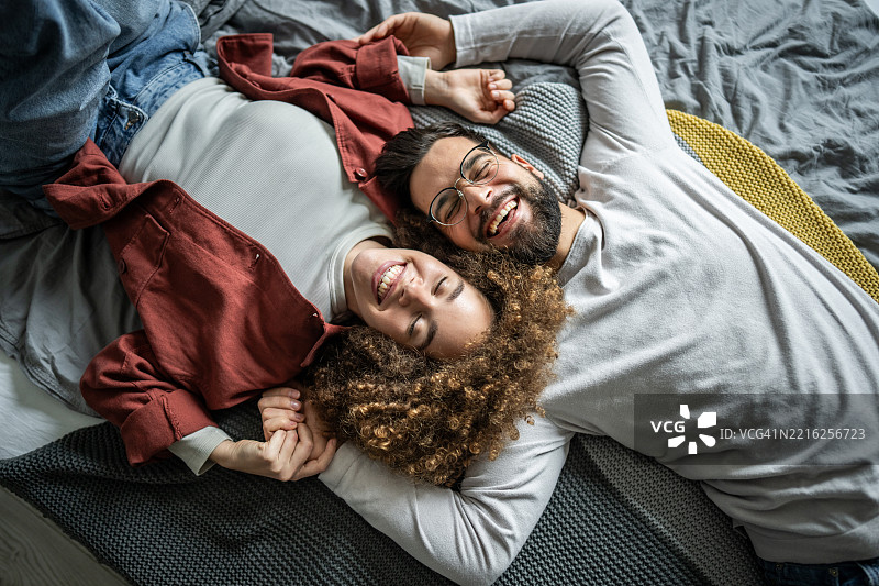 快乐的情侣躺在床上，手牵着手，一起欢笑图片素材