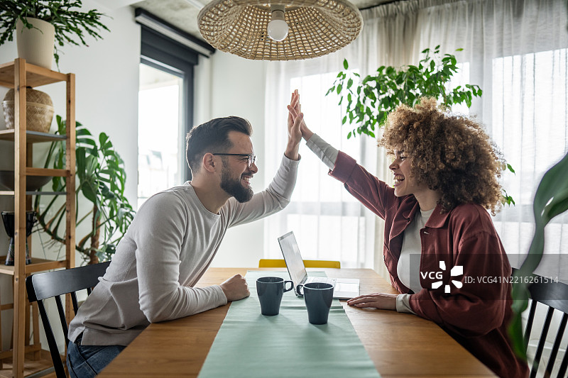 年轻情侣在家工作时击掌庆祝图片素材