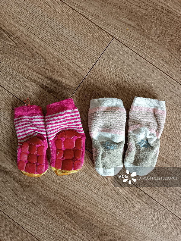 粉色和旧白色的防滑婴儿袜子，柔软温暖，掉落在木地板背景上。图片素材