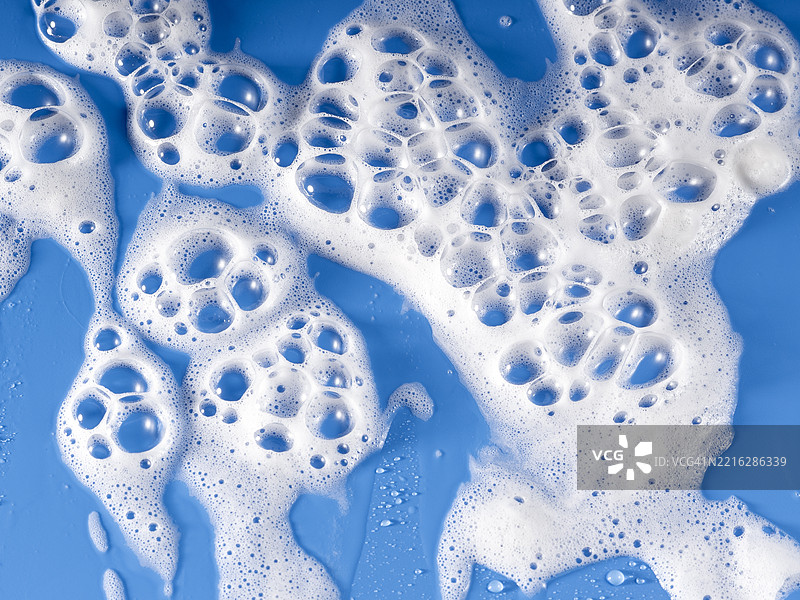 肥皂泡沫与水混合，在蓝色背景上滑动。图片素材