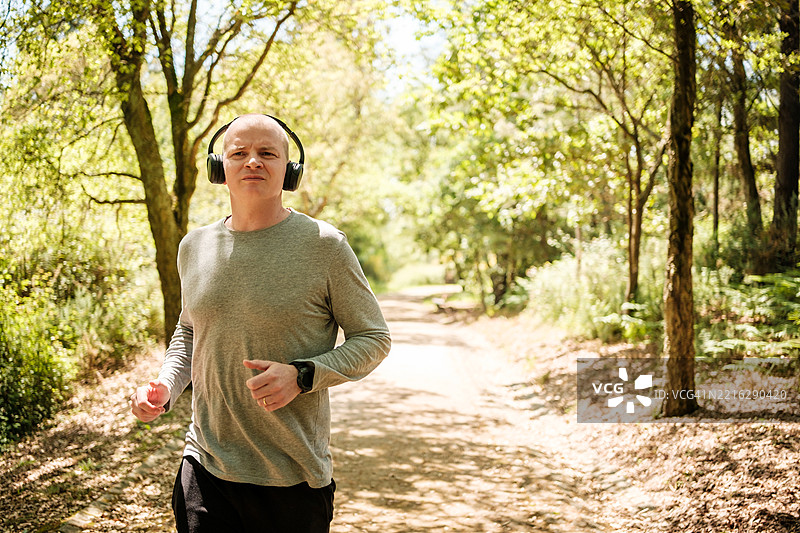 戴着耳机的老年男子在森林小径上慢跑图片素材